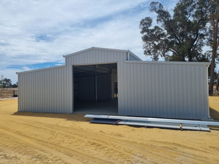 Newly constructed large metal shed on sandy ground.